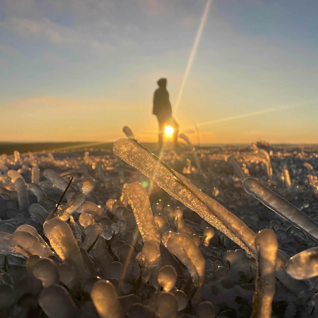 a silhouette with the sun setting between their legs on an icy plateau